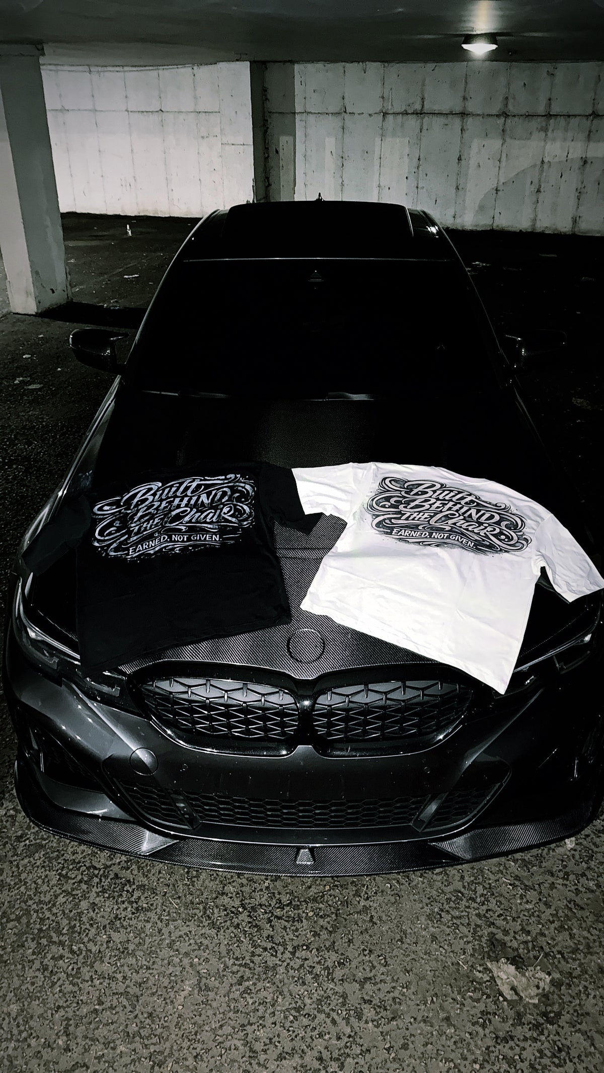 Black and white Built Behind the Chair graphic T-shirts displayed together on a car hood